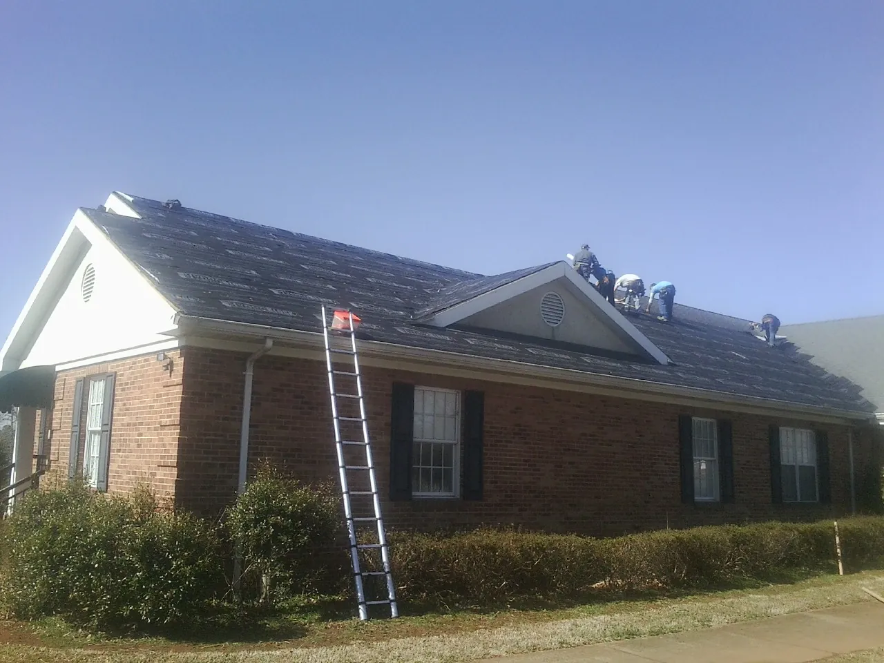 Crew tearing shingles off a brick ranch roof with a ladder set — Emergency Roof Repair work by our crew in Awendaw
