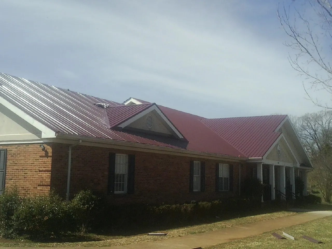 Red metal roof with gabled entries on a long brick building, from a Hail Damage Roof Repair job in Awendaw
