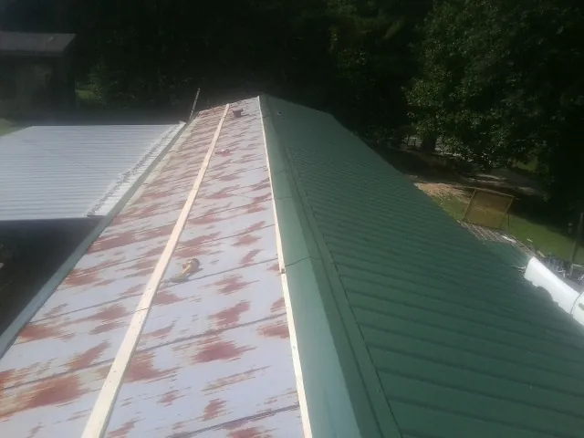 Old rusted panels beside newly installed green metal roofing — Wind Damage Roof Repair by Roofing Brothers in Awendaw