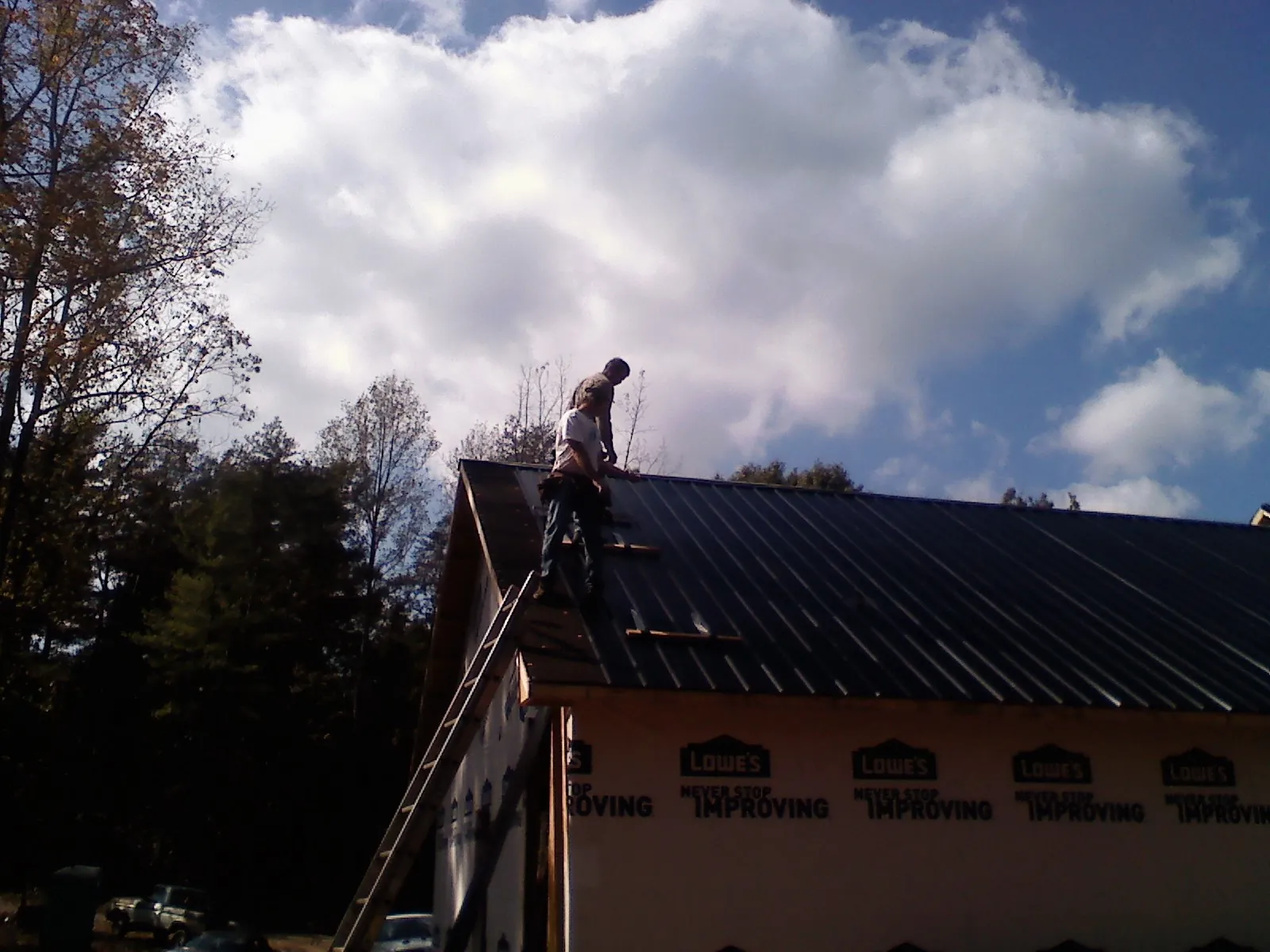 Roofer fastening dark metal panels high against a cloudy sky, from a Roof Inspection job in Awendaw