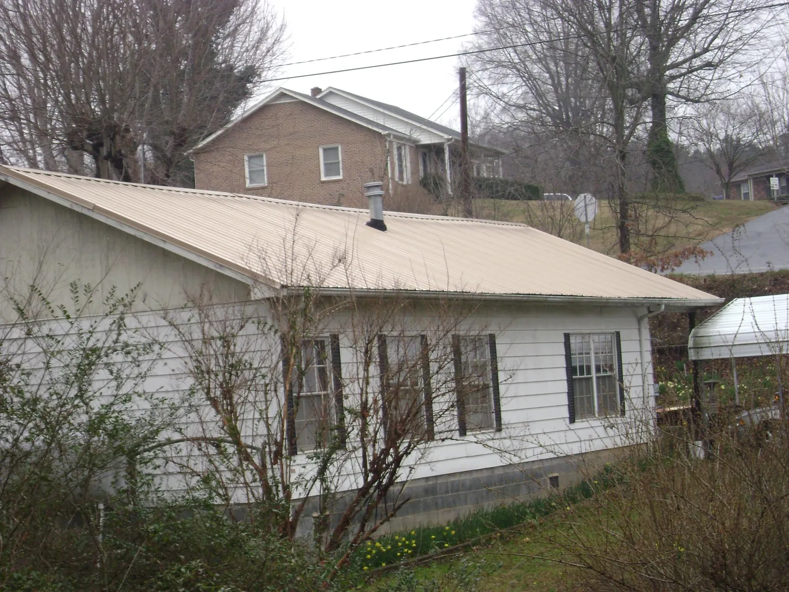 Tan metal roof on a white sided house set into a hillside — Commercial Roofing by Roofing Brothers in Awendaw