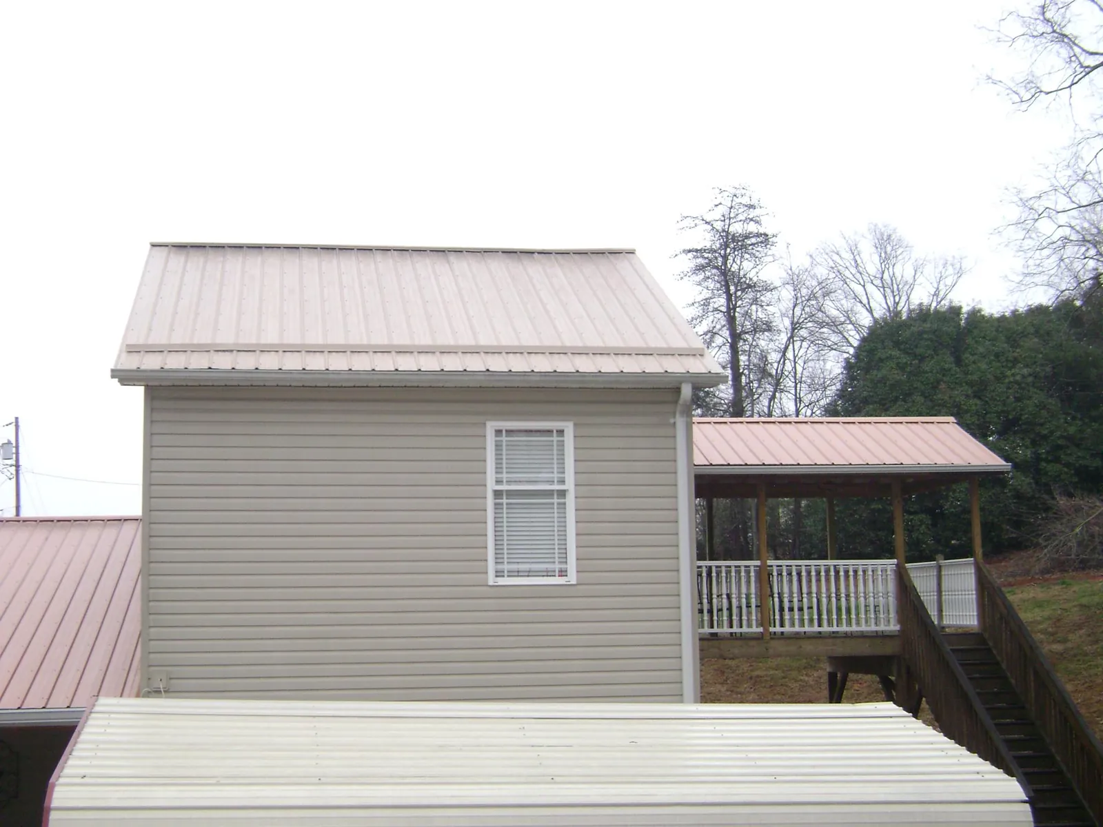 Tan metal roofs on a two story addition and attached porch, from a Roof Replacement job in Awendaw